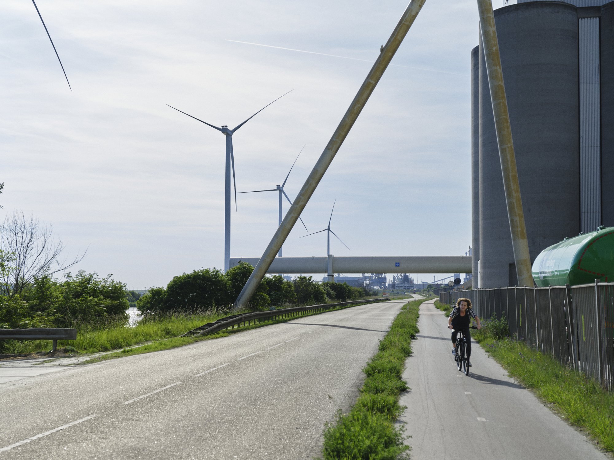 Fietser fietst langs windmolens op bedrijventerrein in IJmuiden