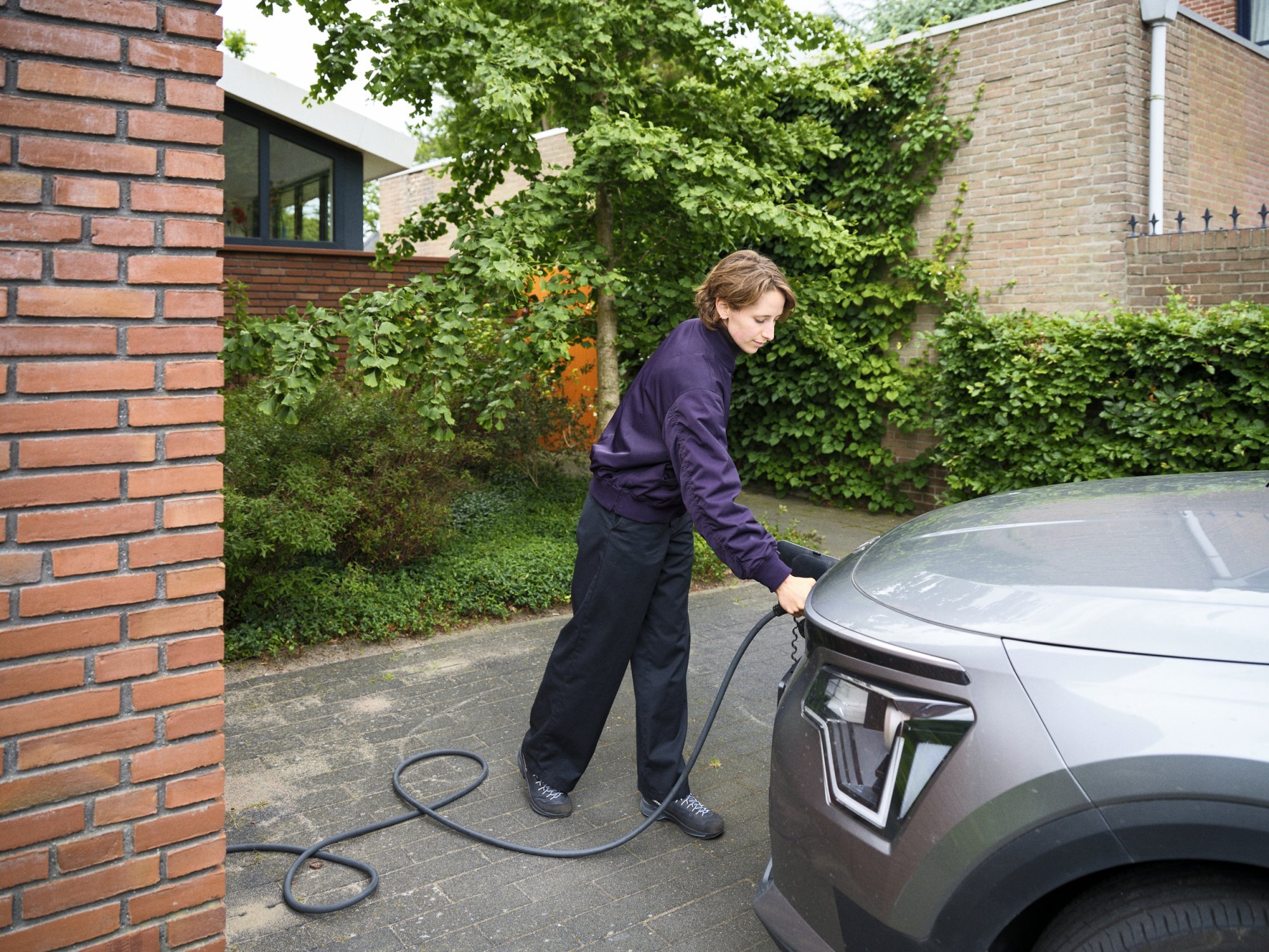Persoon laadt een elektrische auto op bij een woning