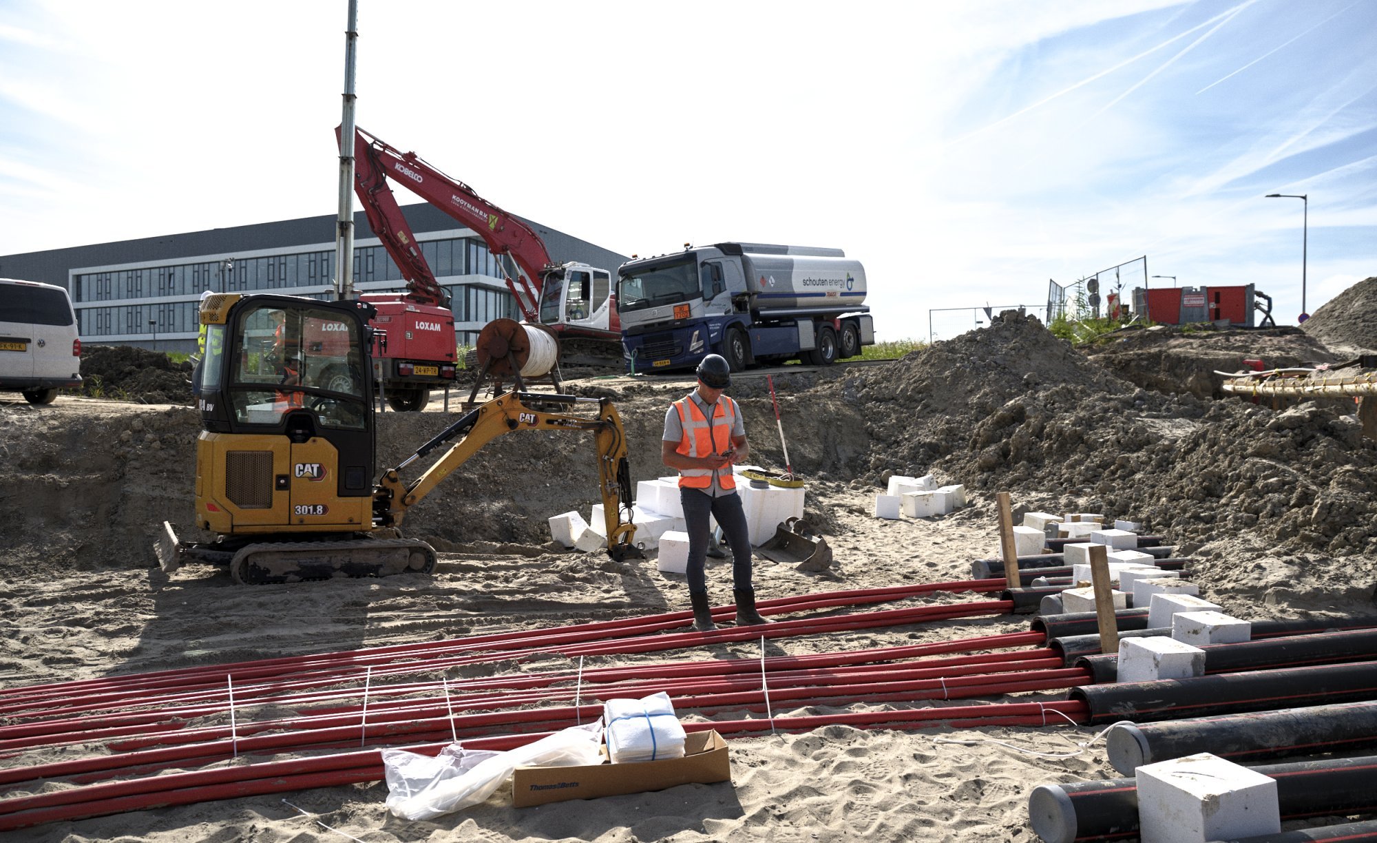 Monteur werkt tussen elektriciteitskabels op een bouwplaats met machines op de achtergrond.