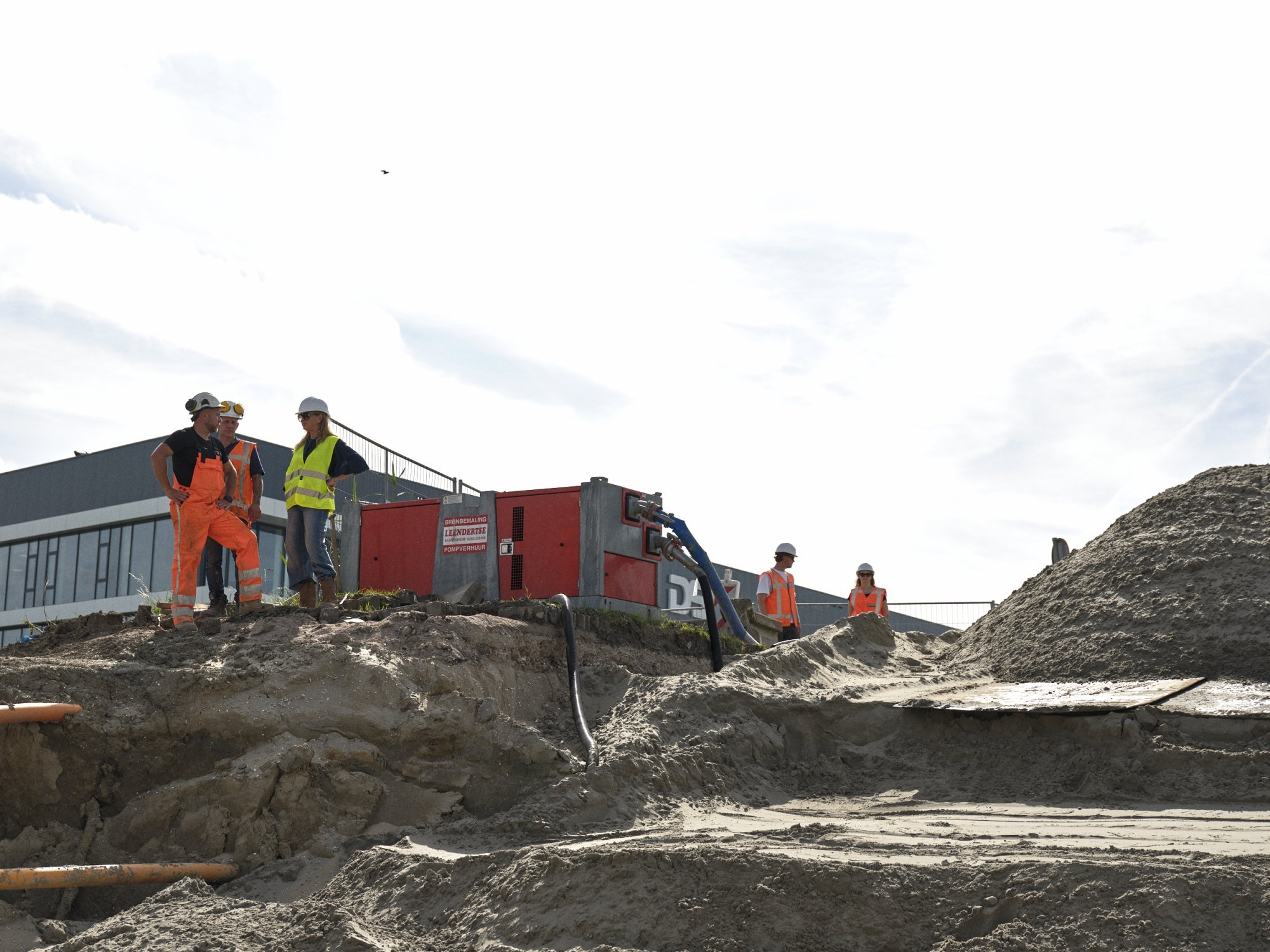 Medewerkers in veiligheidskleding overleggen aan de rand van een bouwput.