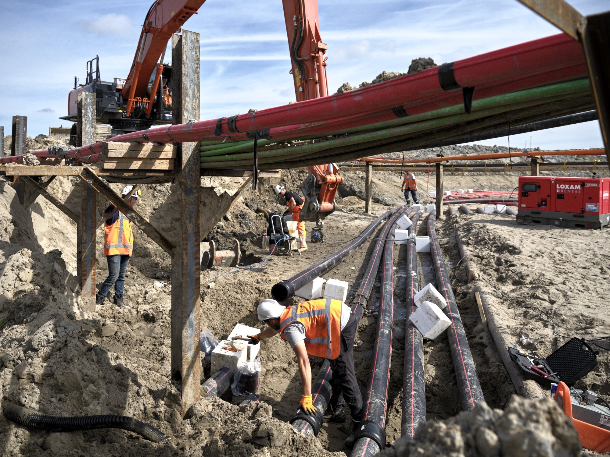 Werkers leggen kabels in een sleuf onder een tijdelijke constructie.